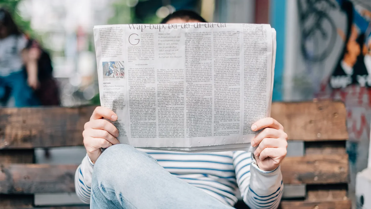 Person reading newspaper on bench outdoors