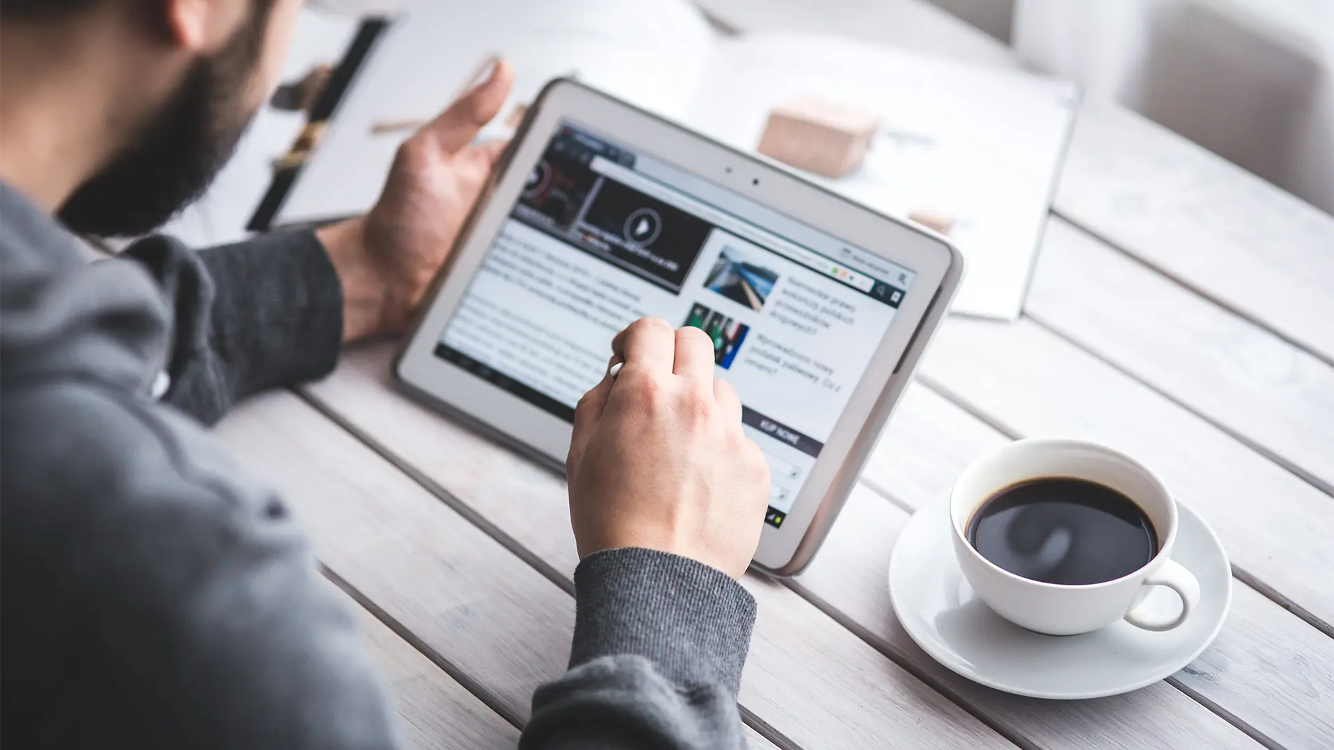 Person reading morning news off of tablet with coffee