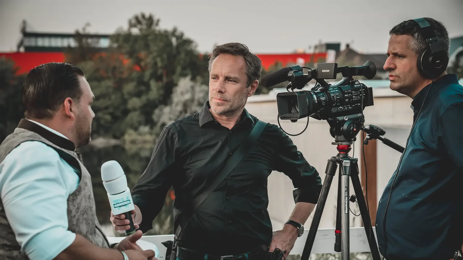 Newscaster and cinematographer interviewing a man outdoors
