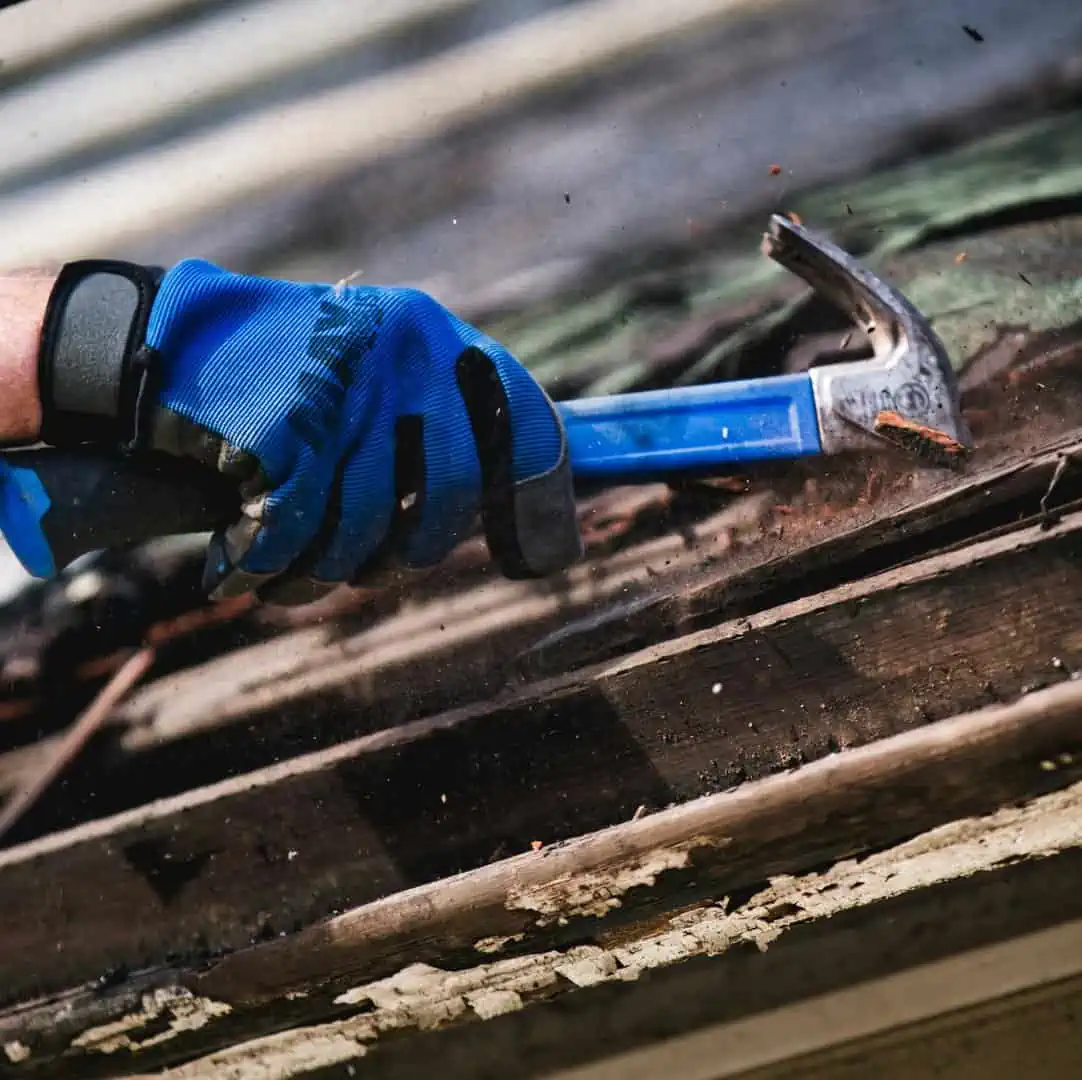 Worker driving a hammer through rotten wood